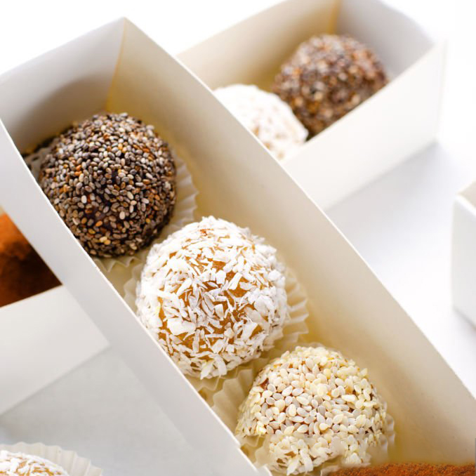 Assorted vegan sweets, Delicious Candy Balls with seeds, dried fruit and cocoa powder, Healthy Candies with Chia, Sesame Seeds, Coconut and Truffles in cardboard boxes on bright background